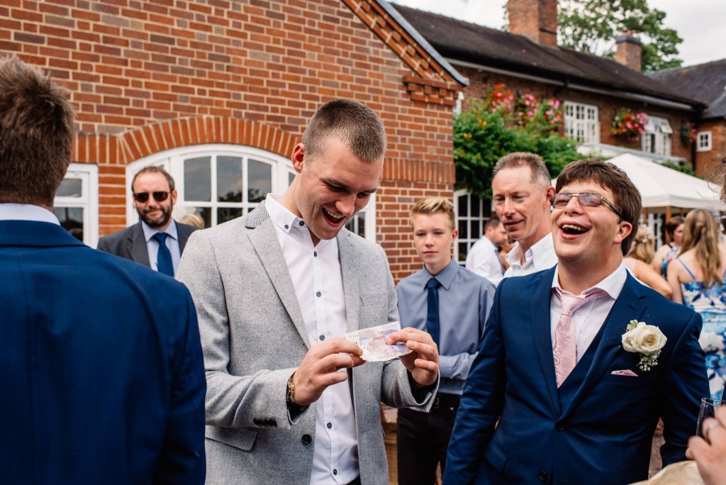 Groomsmen in fits of laughter at close-up card magic outside